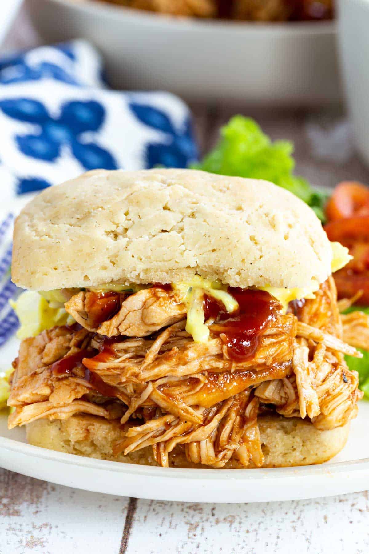 A BBQ pulled chicken sandwich on a plate with a side salad.