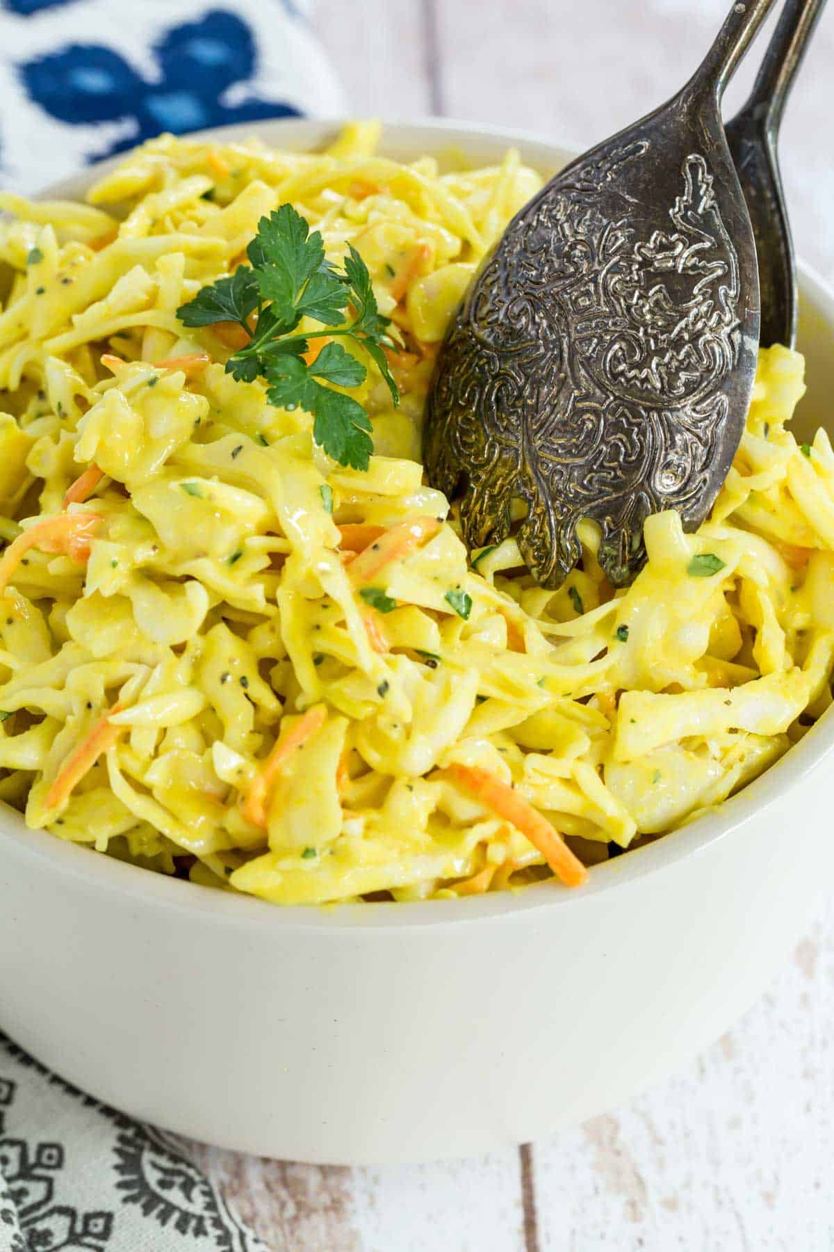 A bowl of mustard coleslaw with salad tongs.