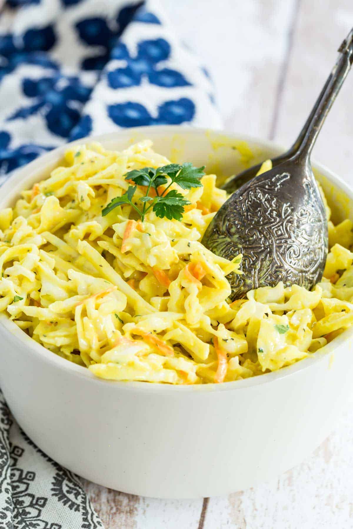 A bowl of mustard coleslaw with salad tongs.