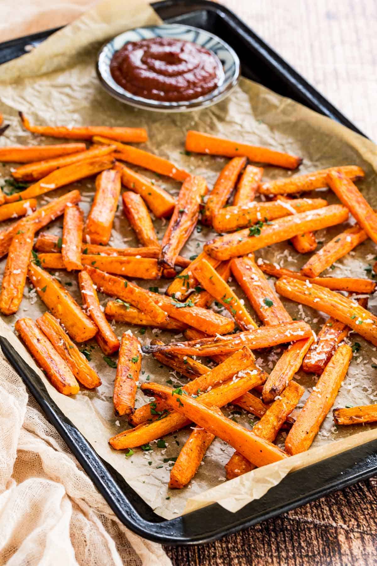 Air fryer carrots on a baking sheet next to ketchup for dipping.