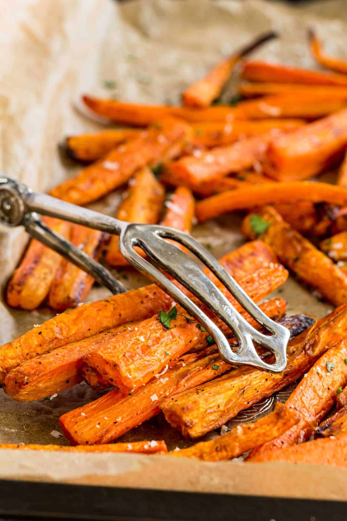 Tongs are used to pick up a serving of air fryer carrots from a baking sheet.