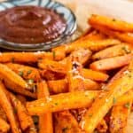 Air fryer roasted carrots on a plate next to a small bowl of ketchup.