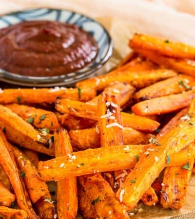 Air fryer roasted carrots on a plate next to a small bowl of ketchup.