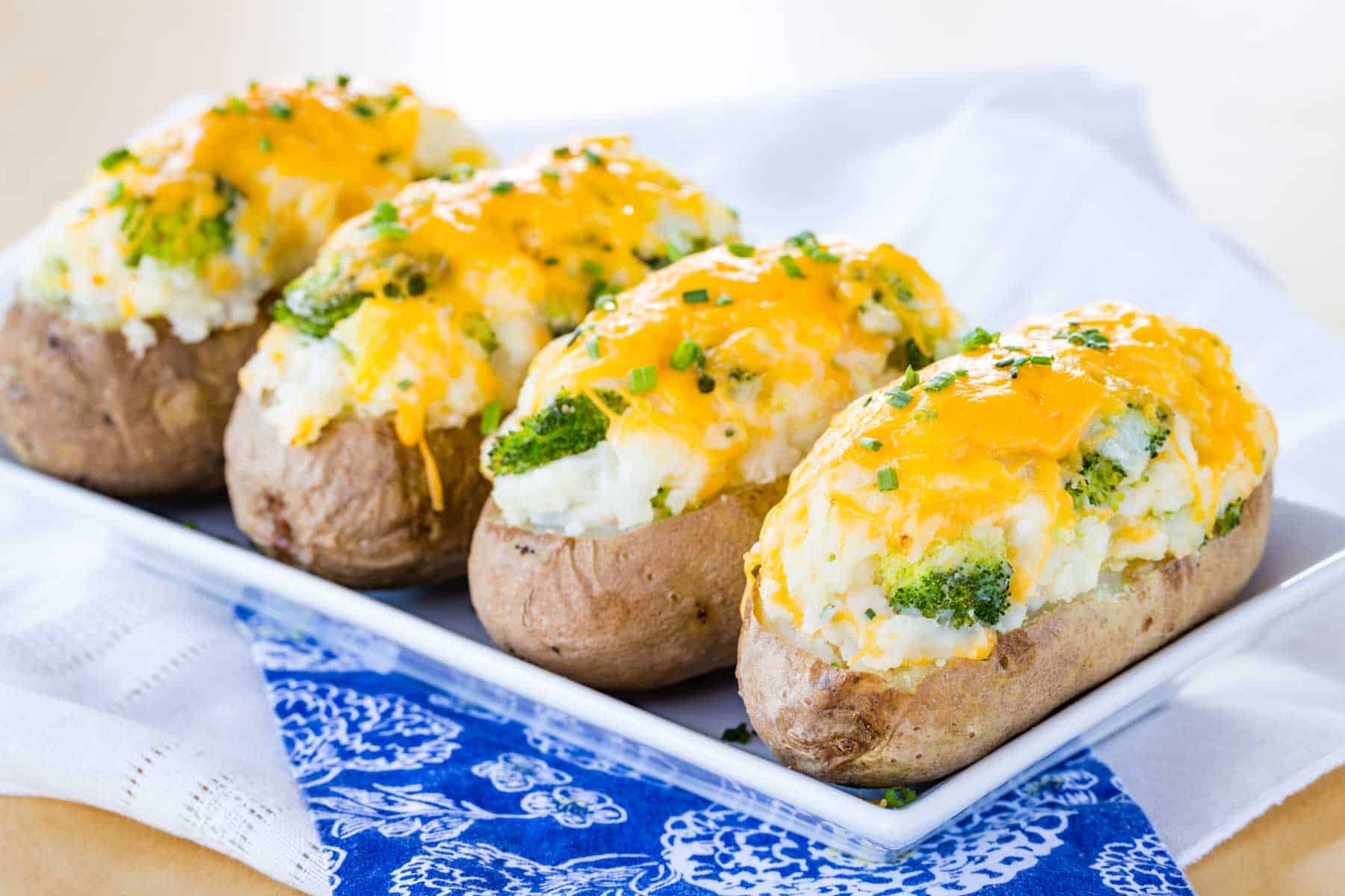 A rectangular white plate with a line of four stuffed potatoes with broccoli.