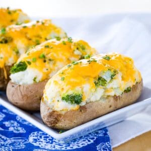 Broccoli Cheddar Baked Potatoes on a white rectangular dish on top of a blue and white napkin.