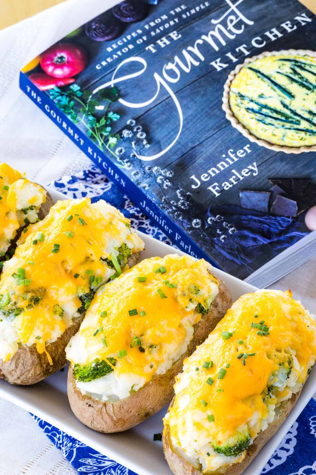Broccoli cheddar baked potatoes on a plate next to The Gourmet Kitchen cookbook.