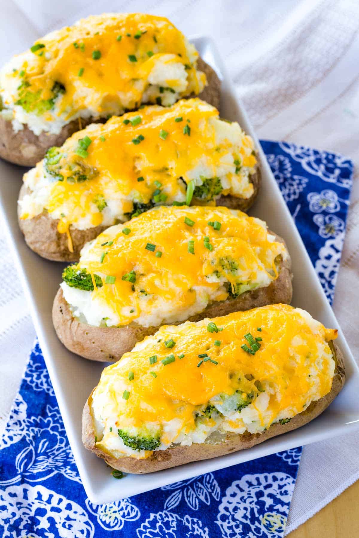 Looking down at the cheesy tops of broccoli cheddar stuffed baked potatoes on a white plate.