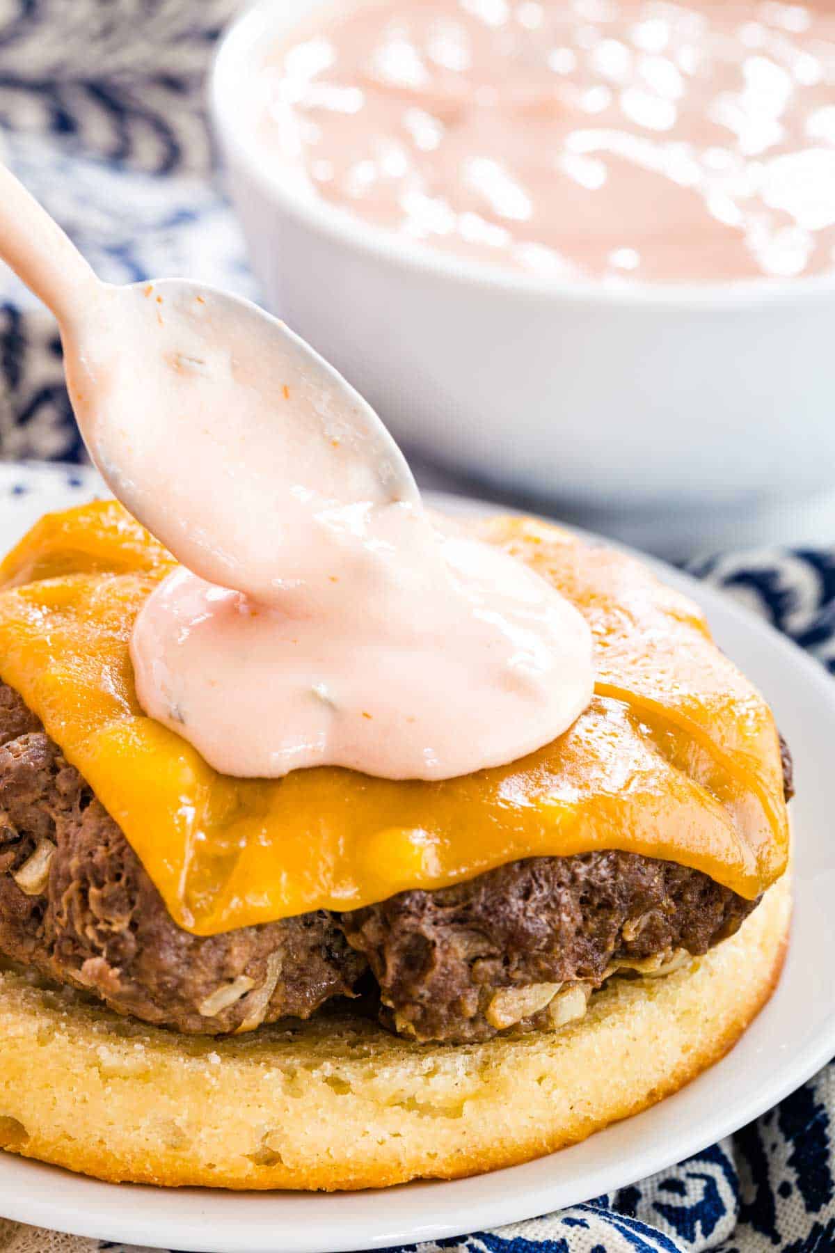 A spoon drops a dollop of Big Mac Sauce onto a cheeseburger patty.