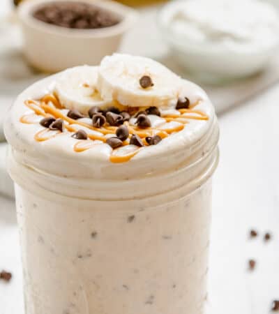 A peanut butter smoothie in a jar topped with banana slices and chocolate chips