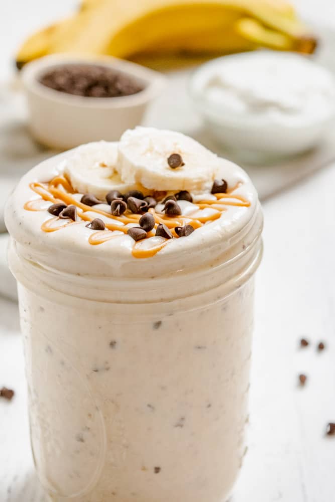 A peanut butter smoothie in a jar topped with banana slices and chocolate chips