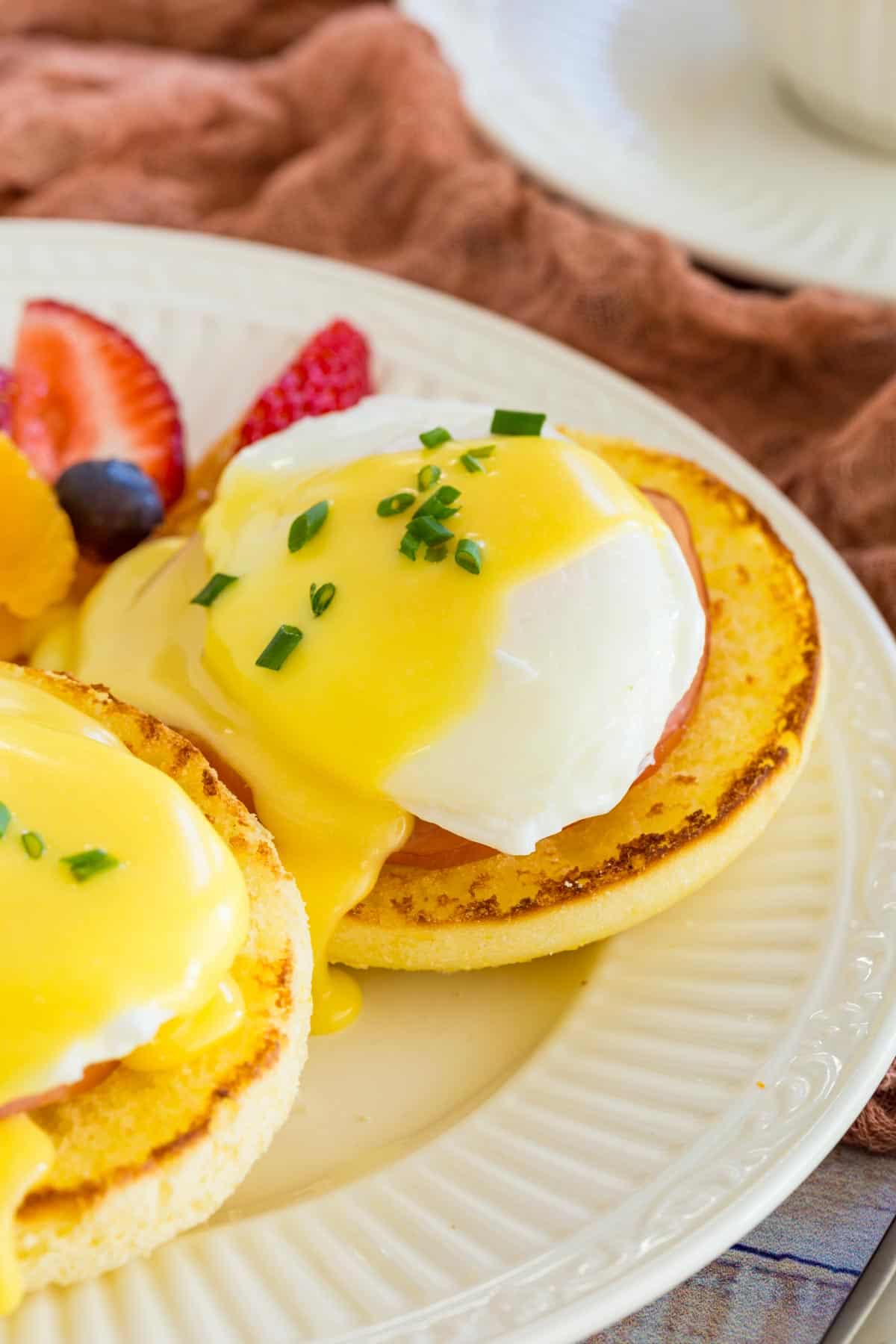 Eggs Benedict on a plate next to fresh cut fruit.