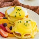 Gluten Free Eggs Benedict on a plate next to fresh fruit.