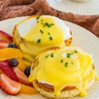 Gluten Free Eggs Benedict on a plate next to fresh fruit.