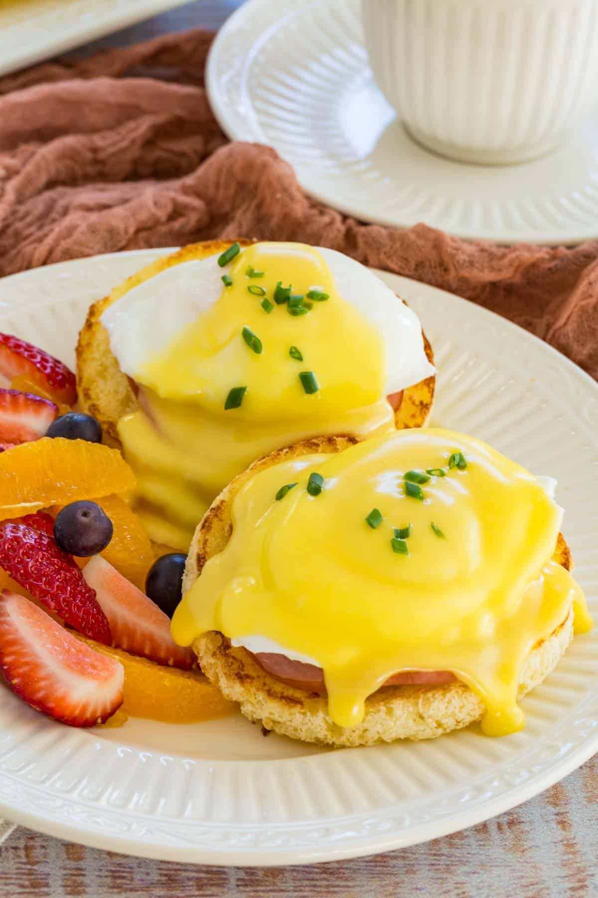 Gluten Free Eggs Benedict on a plate next to fresh fruit.