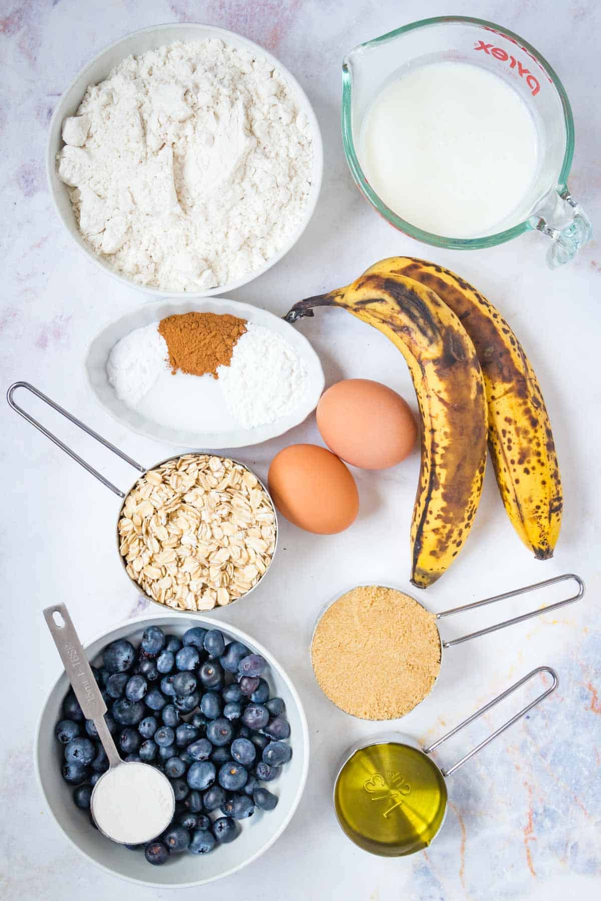 Ripe bananas, gluten-free flour, blueberries and the rest of the muffin ingredients on a countertop