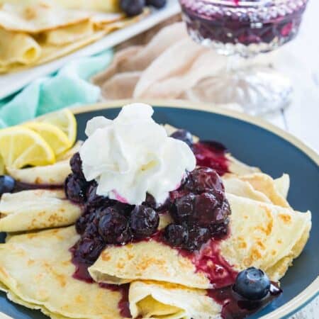 Homemade blueberry crepes topped with a dollop of whipped cream and a few fresh berries