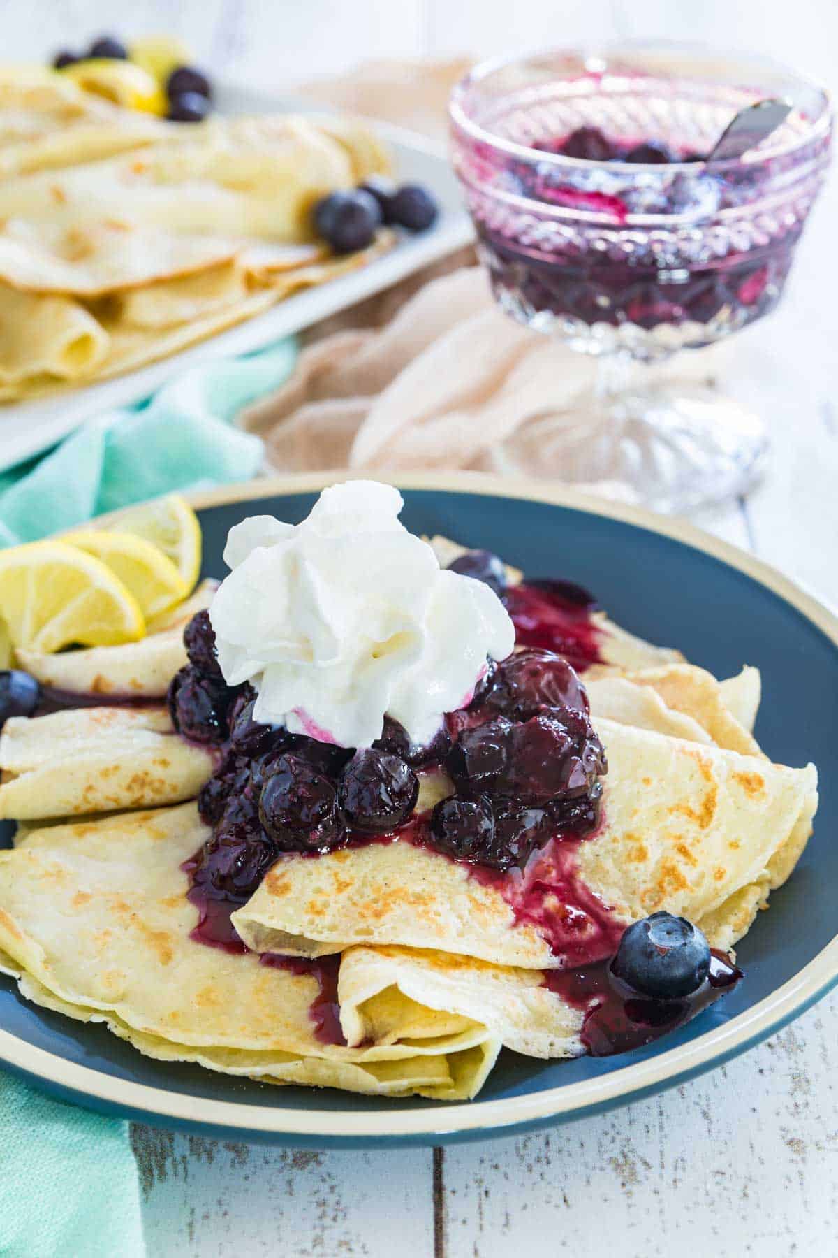 Homemade blueberry crepes topped with a dollop of whipped cream and a few fresh berries