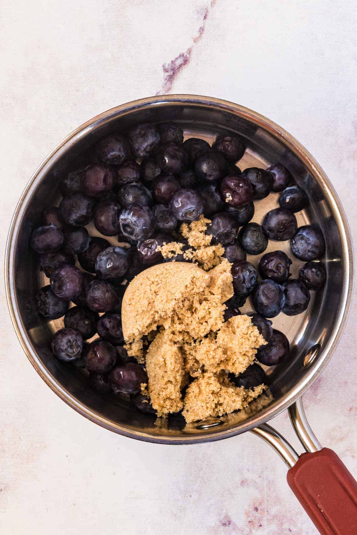 Brown sugar inside of a metal skillet with half a cup of rinsed and dried blueberries