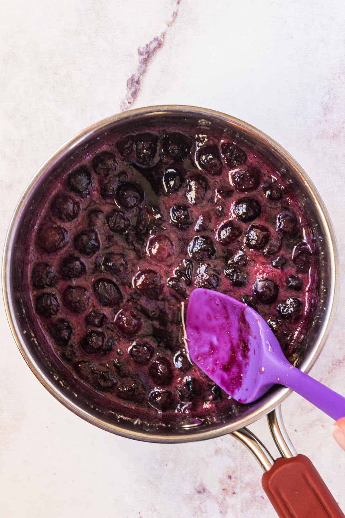 Homemade blueberry sauce being stirred with a purple rubber spatula
