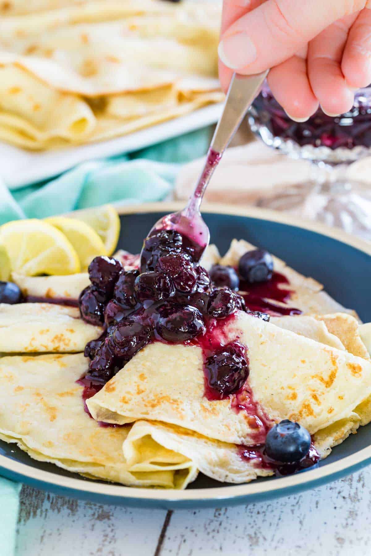 A plate of gluten-free crepes with homemade blueberry syrup being spooned on top of them