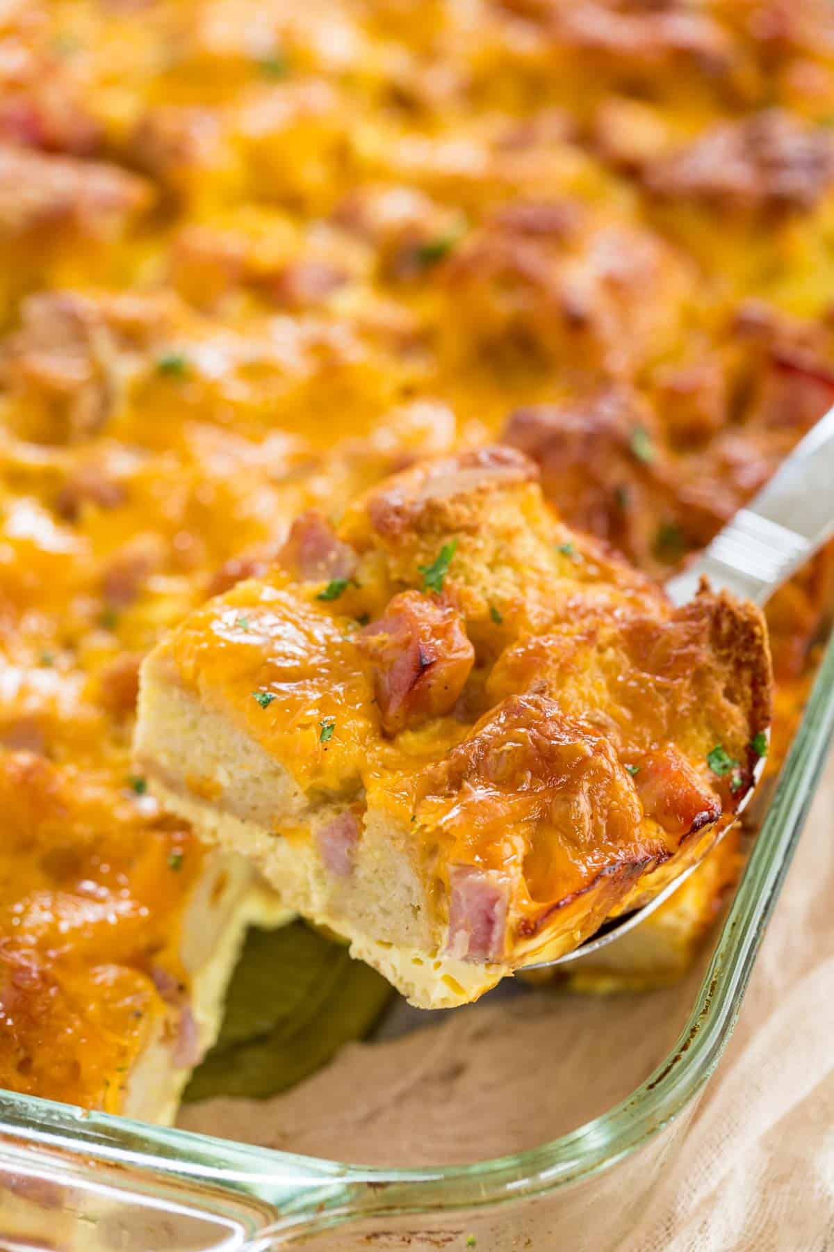 A slice of gluten free ham and cheese strata is lifted from a baking pan.