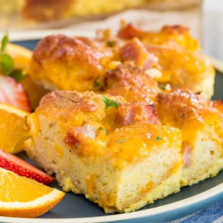 Slices of gluten free ham and cheese strata on a green plate next to fresh fruit.