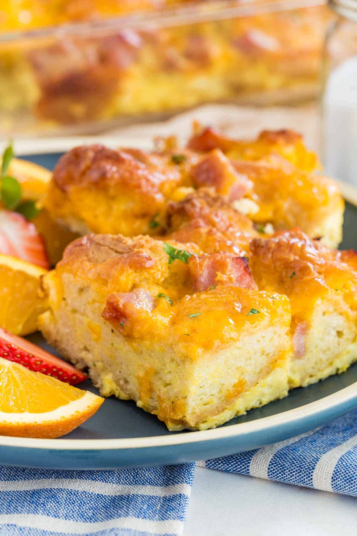 Slices of gluten free ham and cheese strata on a green plate next to fresh fruit.