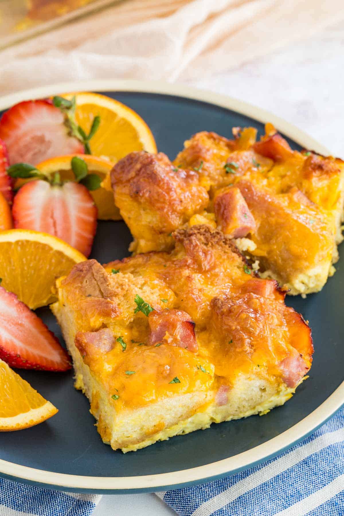 Slices of gluten free ham and cheese strata on a green plate next to fresh fruit.