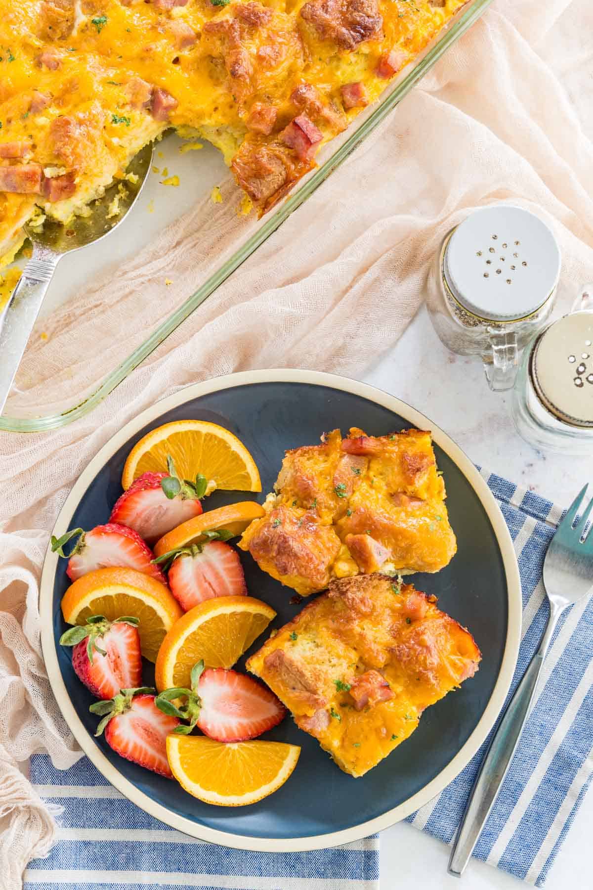 Top view of gluten free ham and cheese strata slices on a green plate next to a casserole dish.