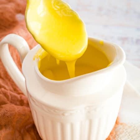 A spoonful of hollandaise sauce drips above a gravy boat.