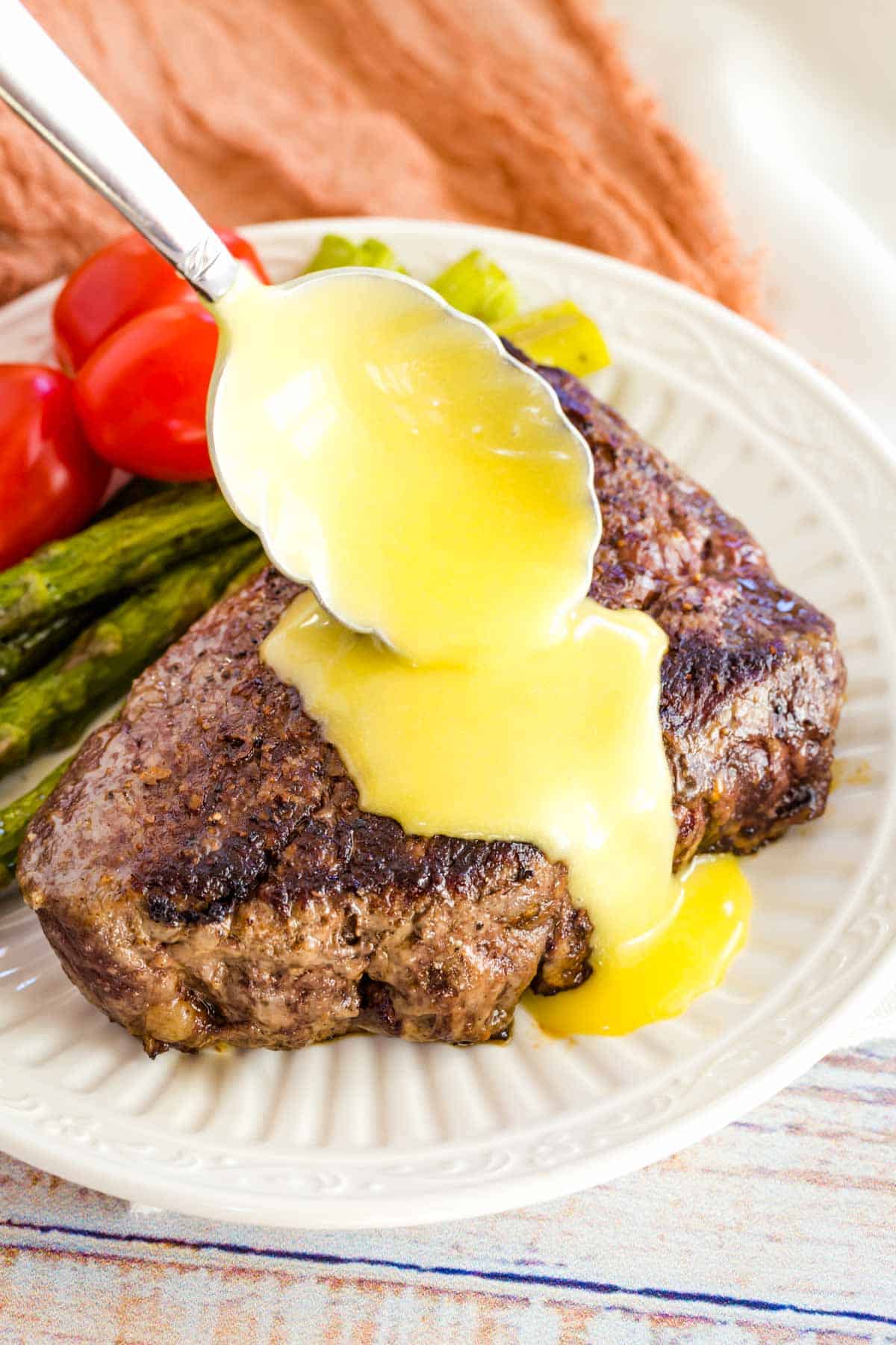 Hollandaise sauce is spooned over top a steak next to veggies.