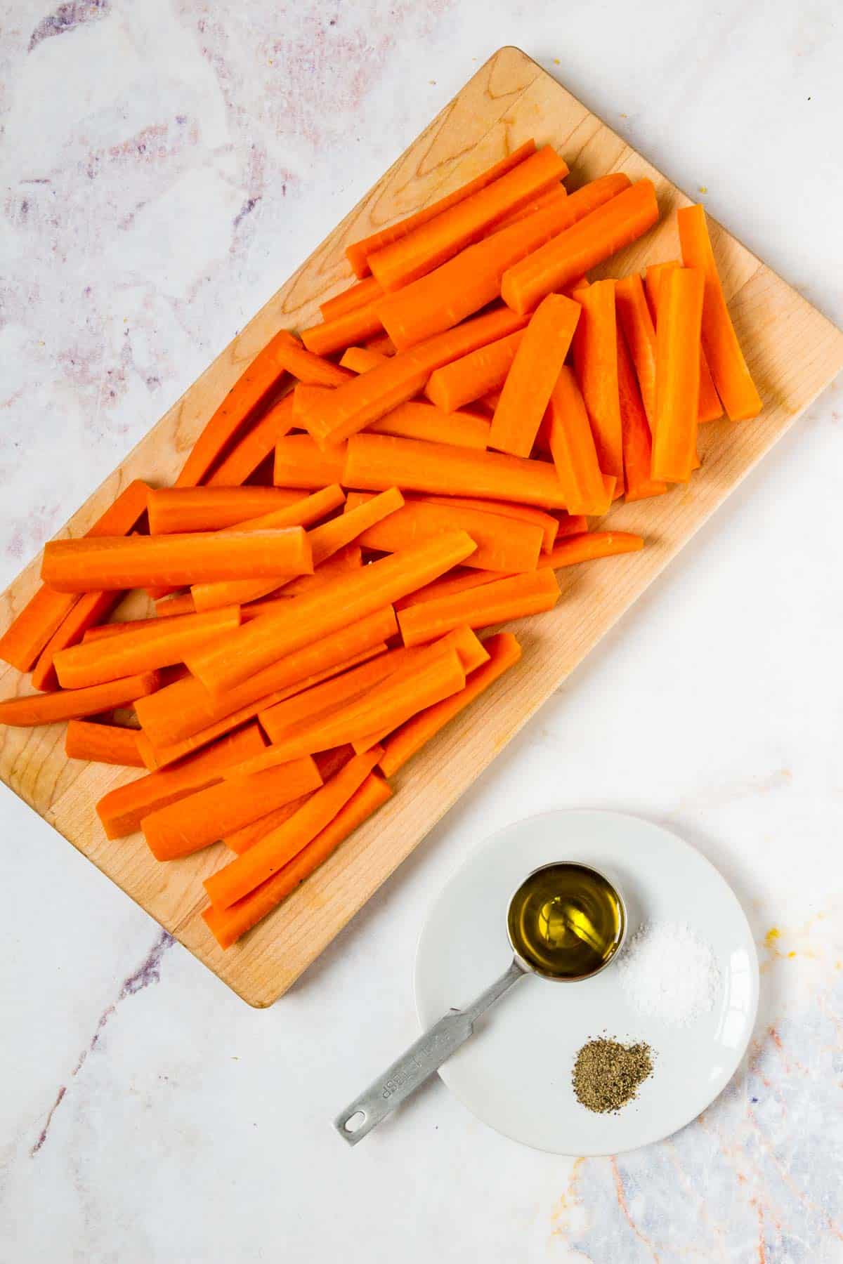 Carrots cut into 2-3 inch sticks on a cutting board next to a tablespoon and seasonings.