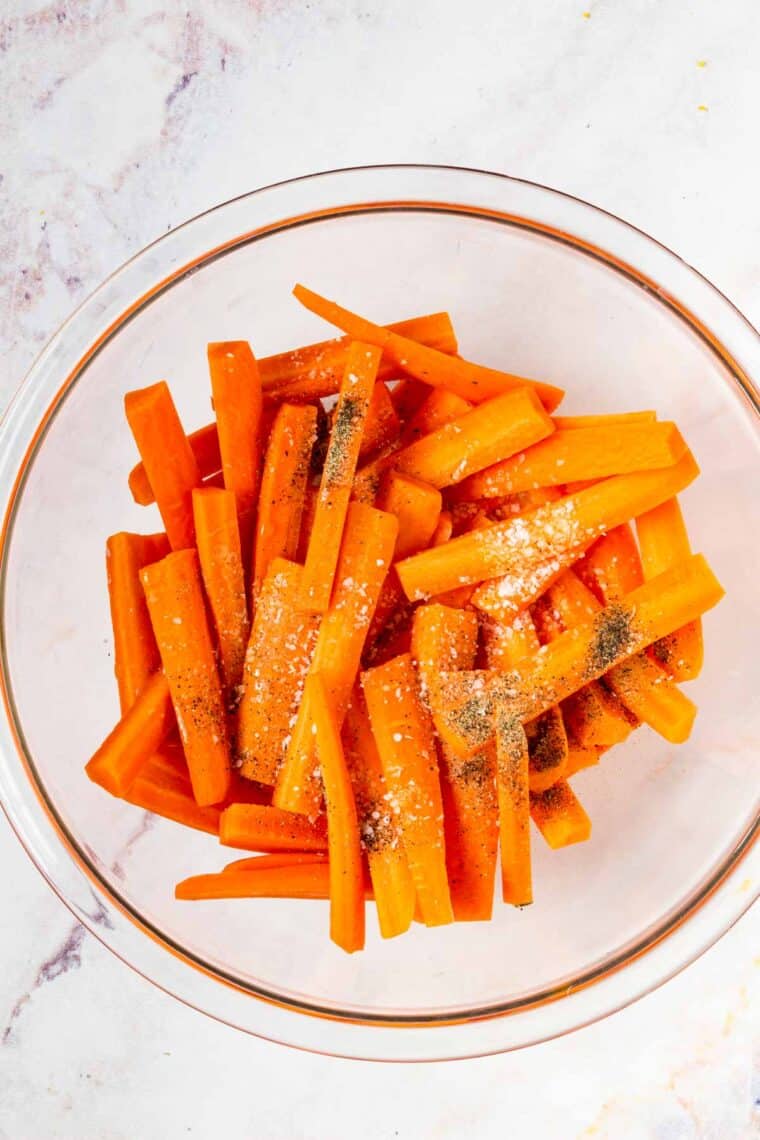 Carrot sticks in a bowl with seasonings and oil.