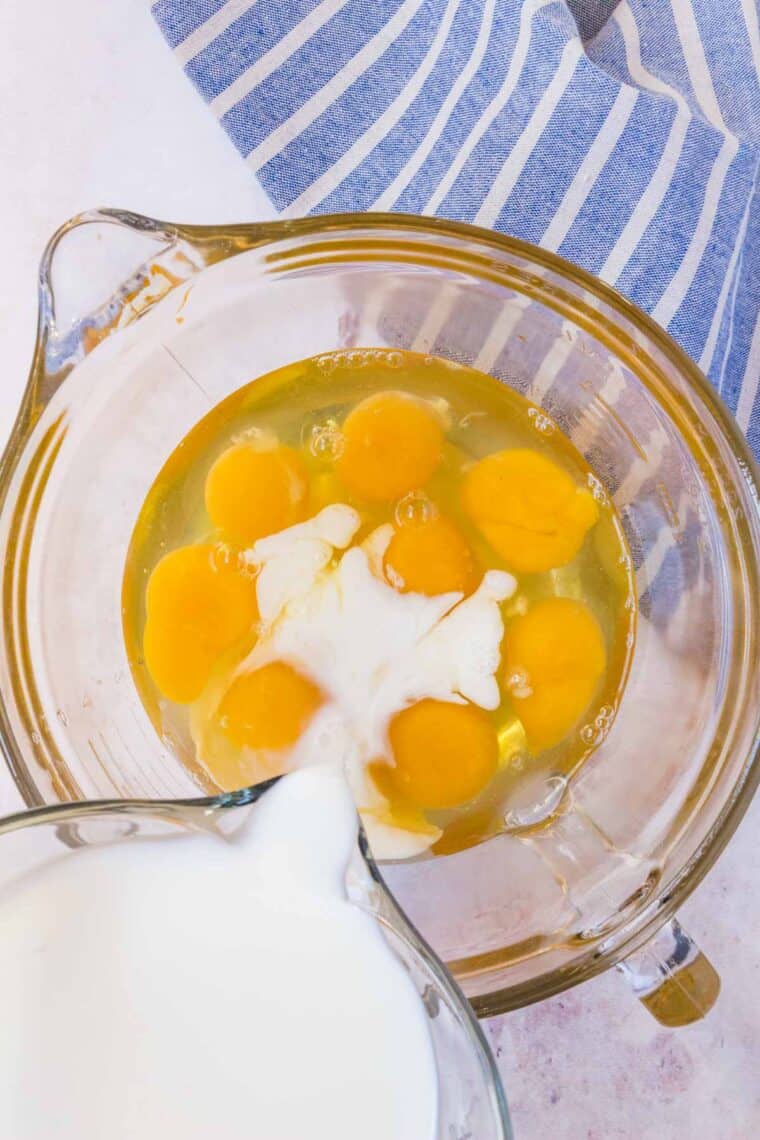 Milk is added into a mixing bowl with eggs.
