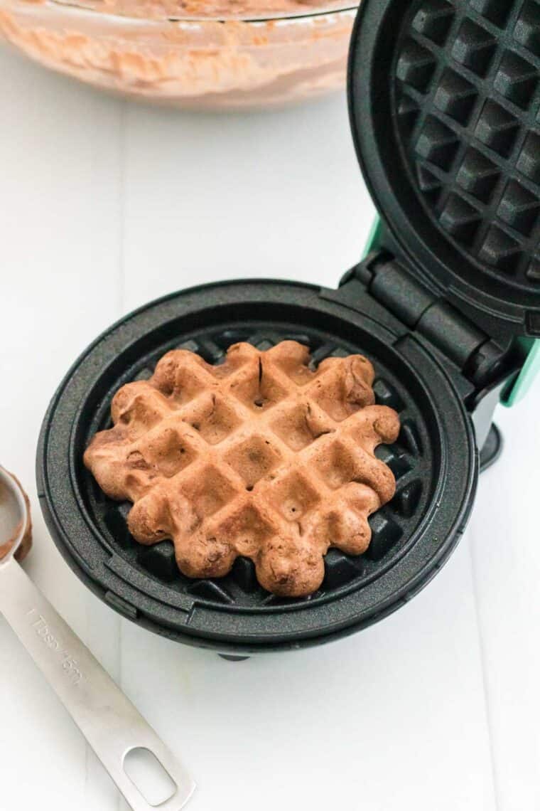 One chocolate waffle cooking in a mini waffle iron.
