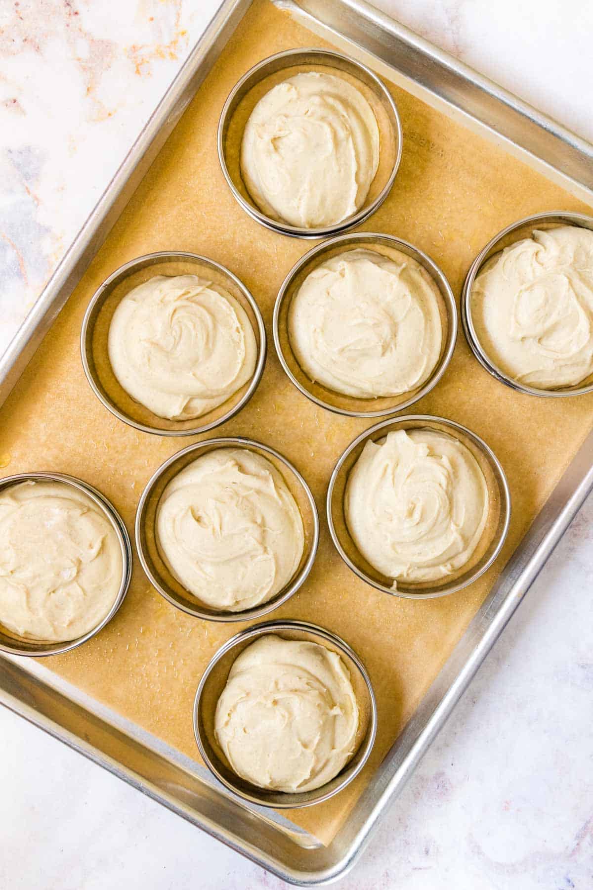 Hamburger bun dough in dough rings on a baking sheet.