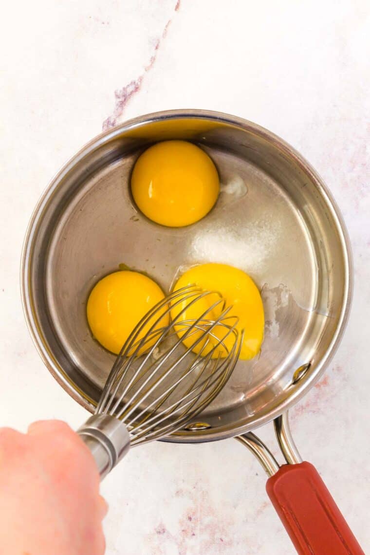 Egg yolks are whisked together in a saucepan.