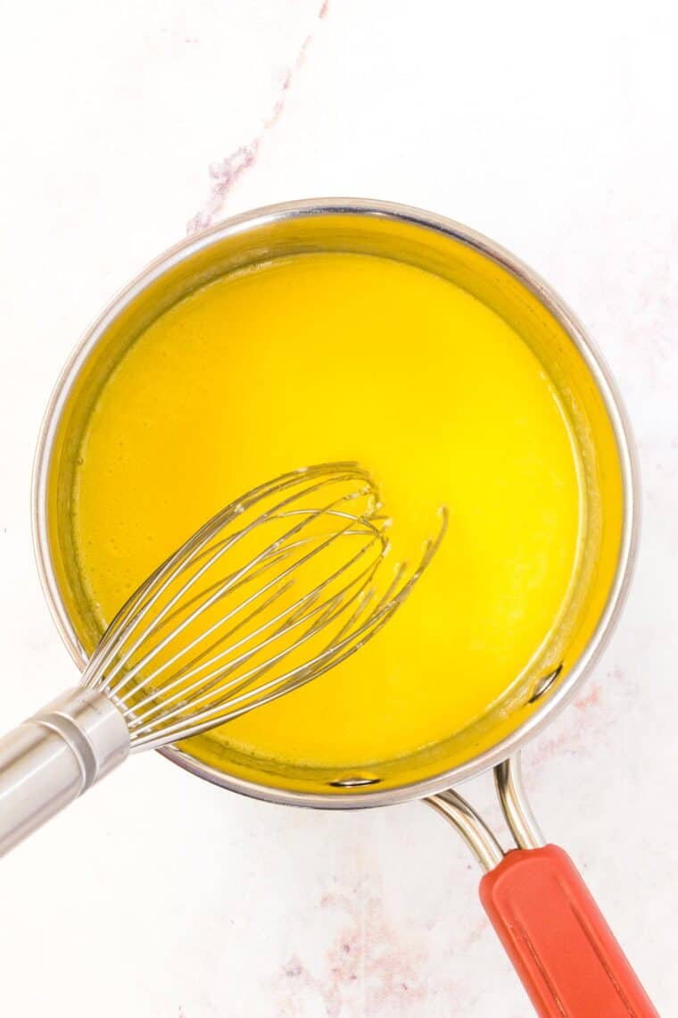 Hollandaise sauce is whisked in a saucepan.