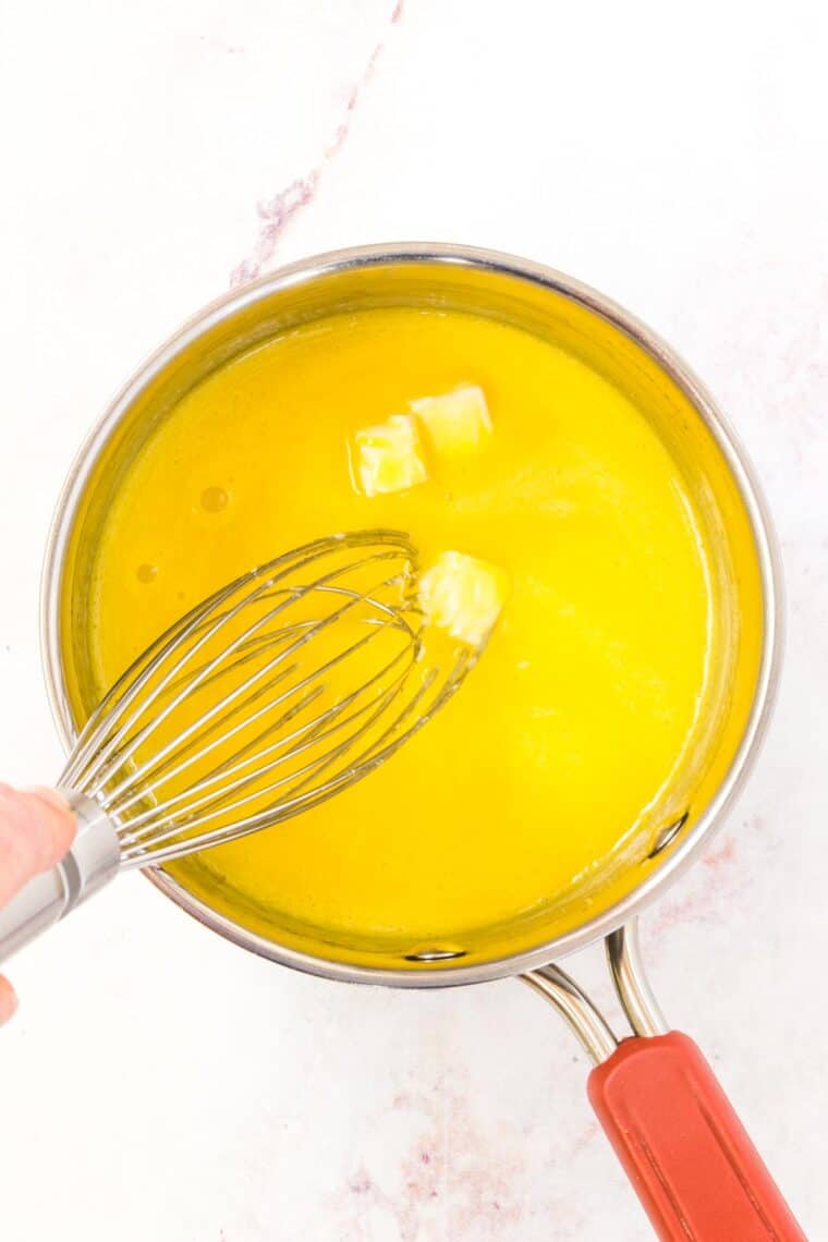 Butter is melted into hollandaise sauce in a saucepan.
