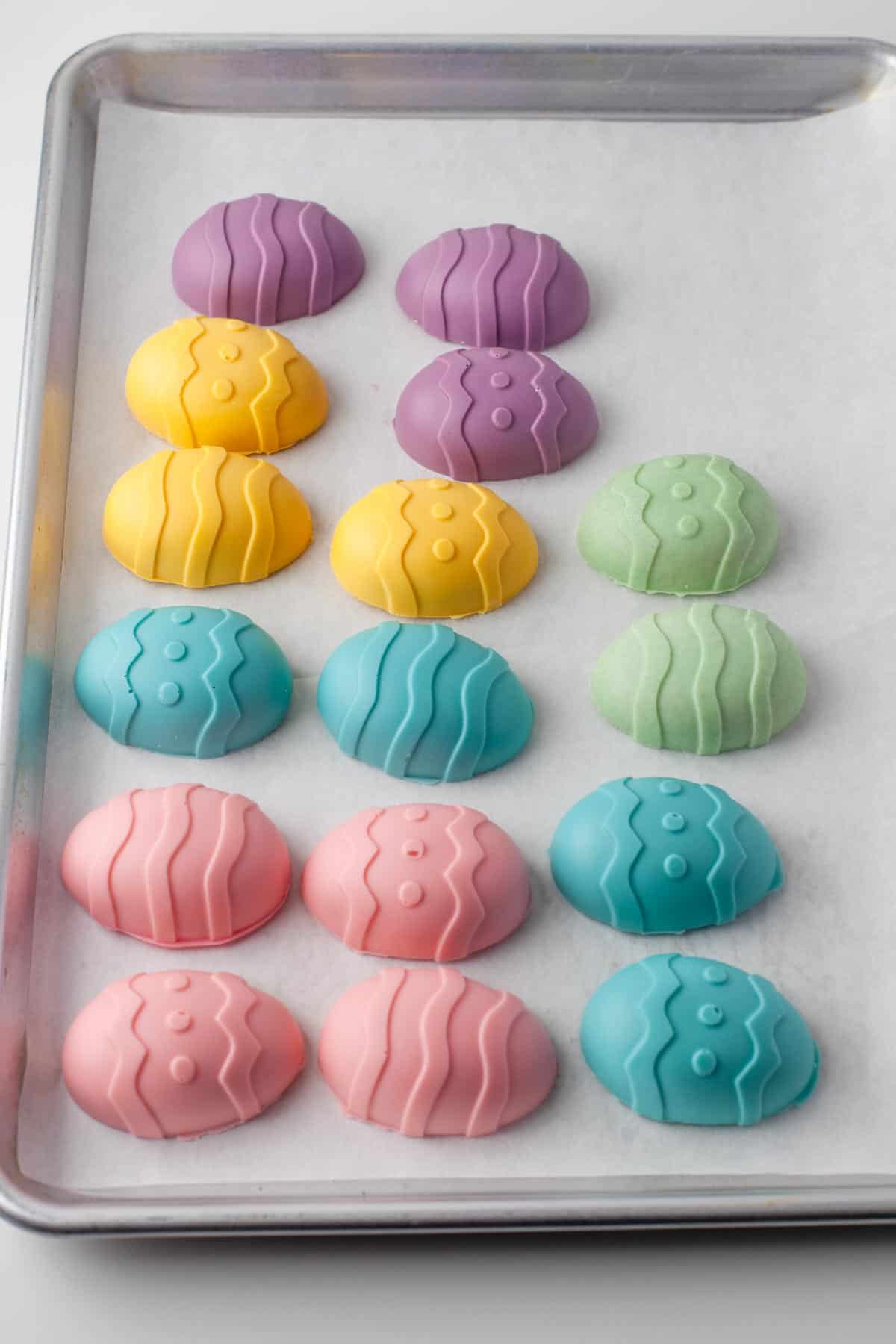 Pastel colored peanut butter eggs on a parchment lined baking sheet.