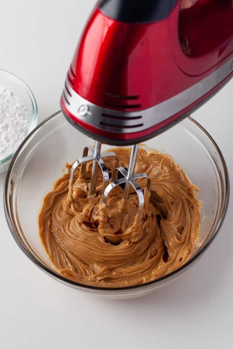 Butter and peanut butter being creamed in a bowl with a hand mixer.