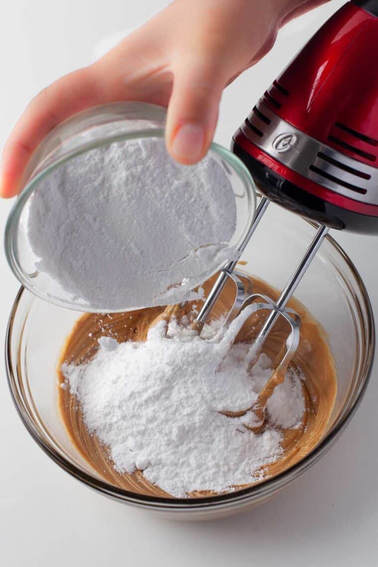 Adding powdered sugar to the peanut butter mixture in a bowl.