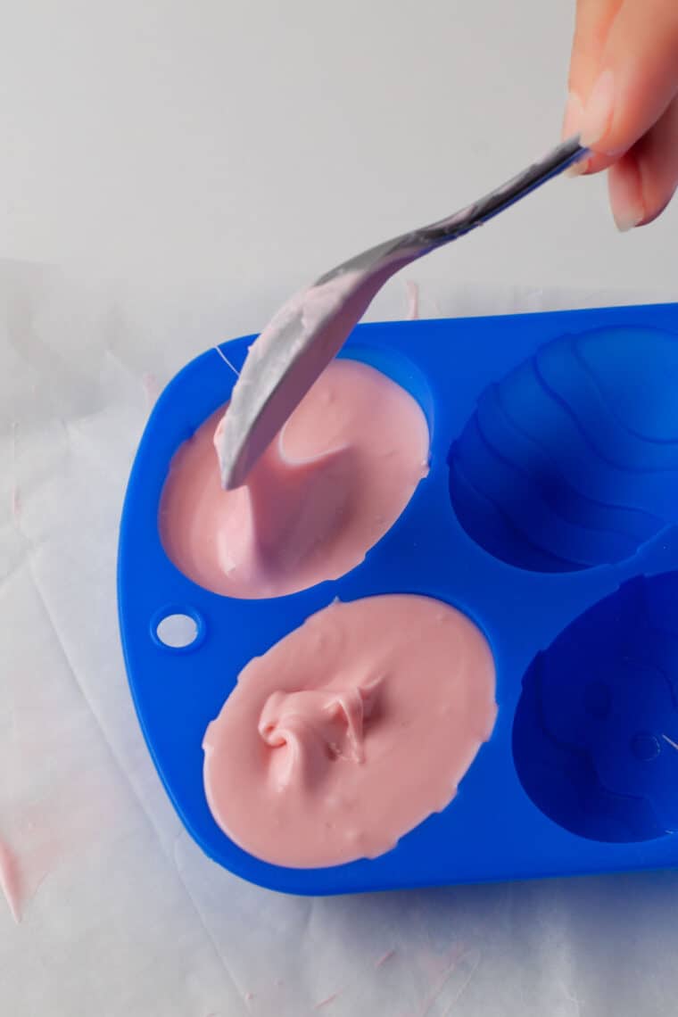 Spooning pink chocolate into an egg-shaped mold.