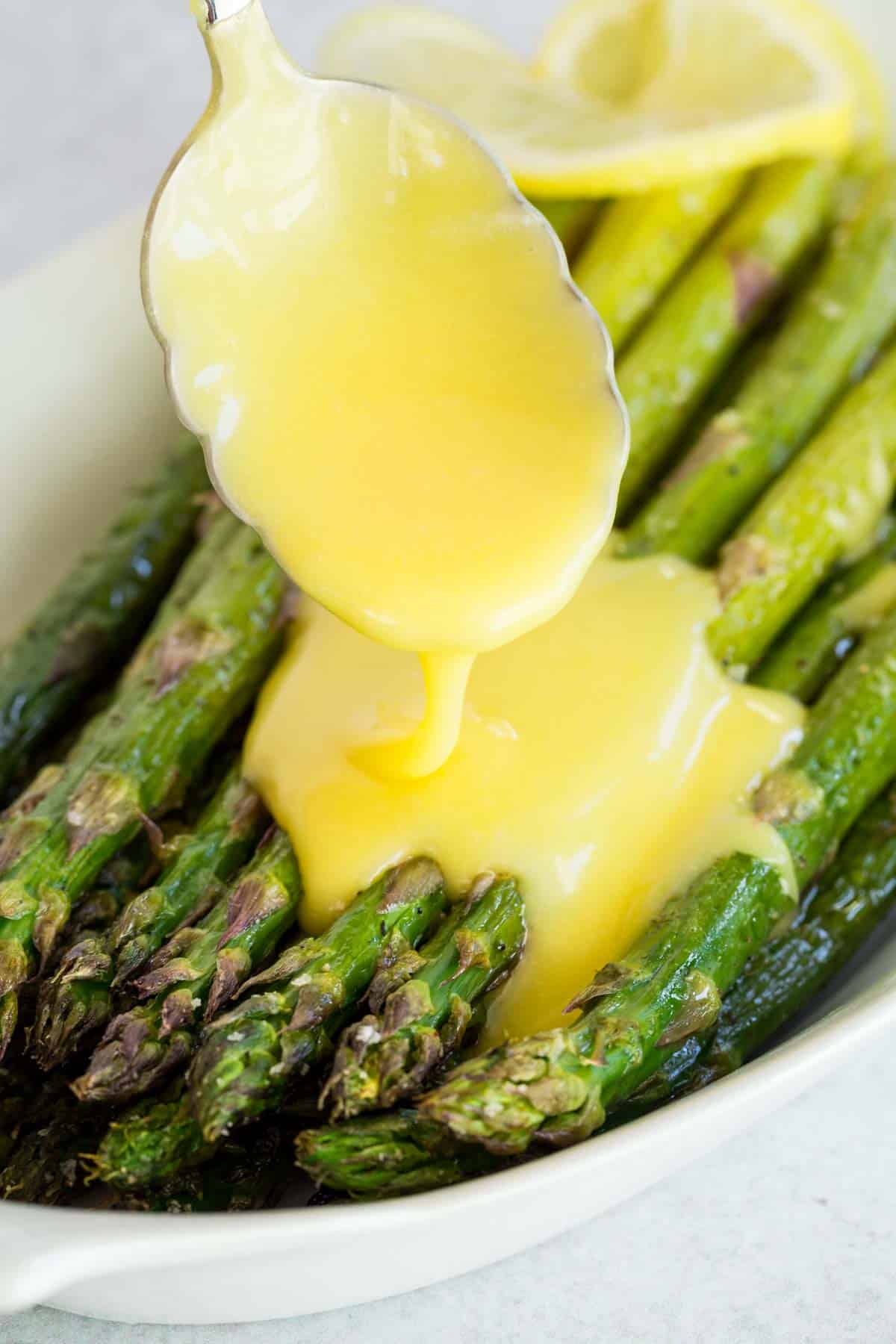Hollandaise sauce is spooned over top a dish filled with roasted asparagus.