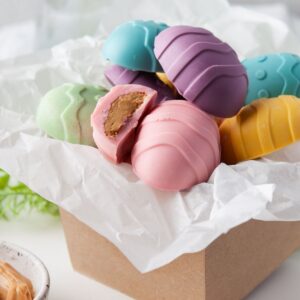 Pastel colored chocolate peanut butter eggs in a parchment lined box.