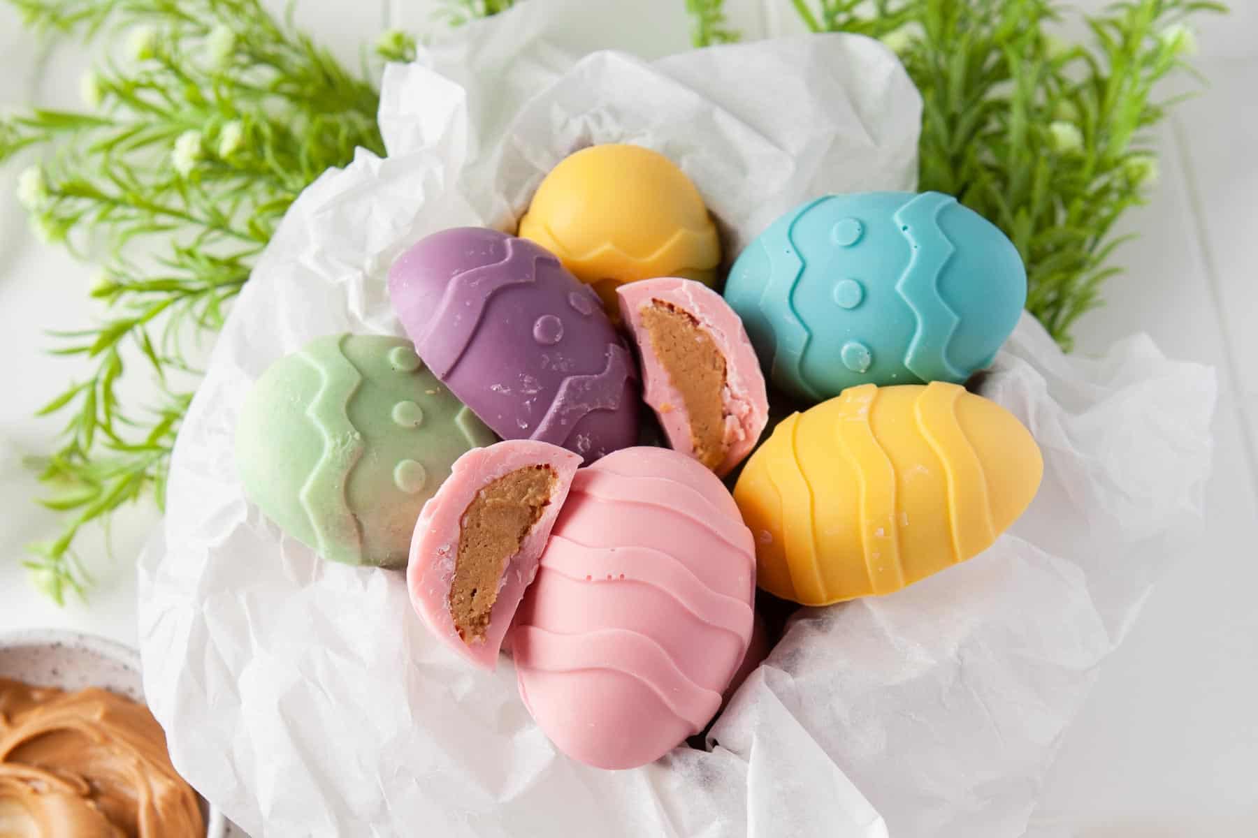 Peanut butter eggs covered in pastel-colored white chocolate with one cut in half.