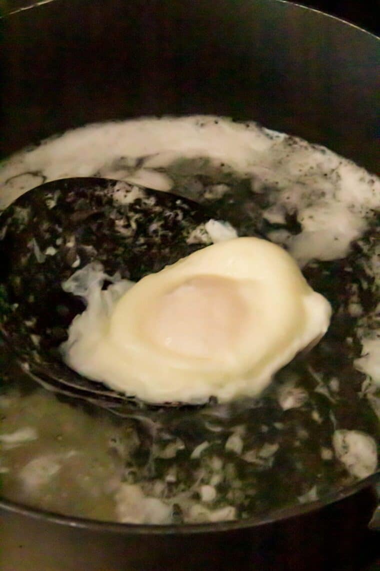 A poached egg in a pan filled with simmering water.