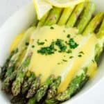 A serving dish with oven roasted asparagus topped with hollandaise sauce with lemon slices.