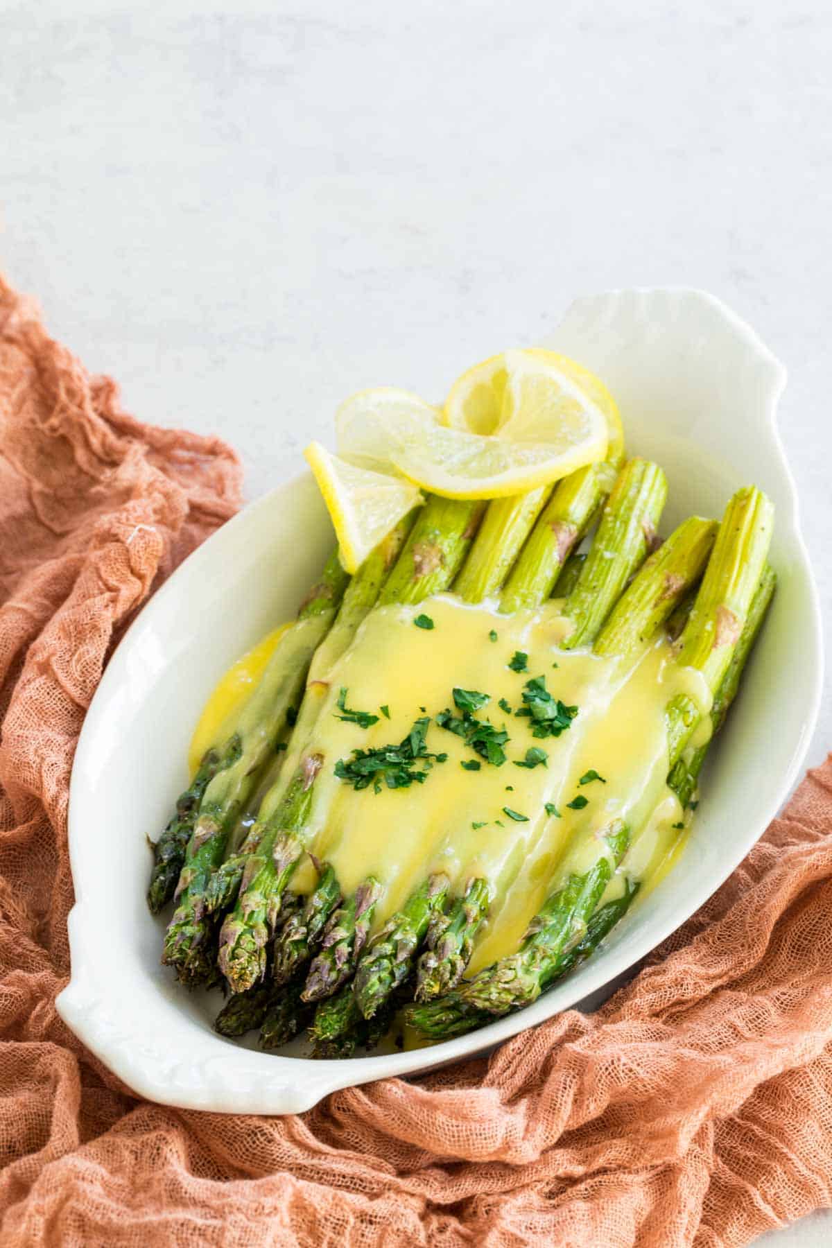 A serving dish with oven roasted asparagus topped with hollandaise sauce with lemon slices.