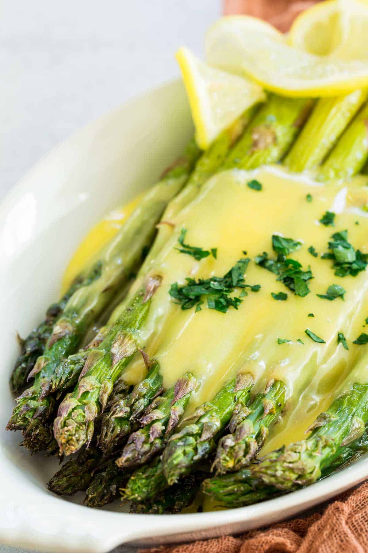 A serving dish with oven roasted asparagus topped with hollandaise sauce with lemon slices.